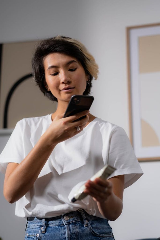 A young woman scans a skincare product with her smartphone camera indoors.